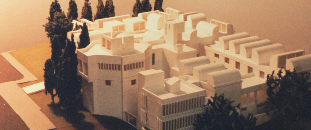 Maqueta arquitectónica en color blanco que representa un edificio de volúmenes complejos y formas curvas, acompañada de árboles a escala en los alrededores.